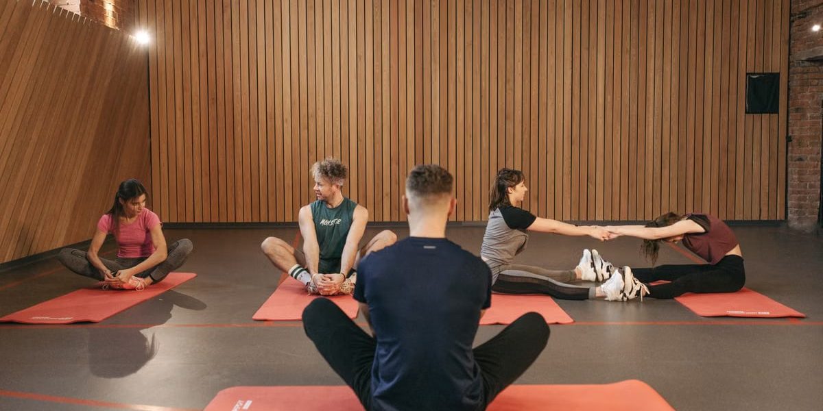 A group of adults practicing yoga and stretching on mats in a wooden panelled room.