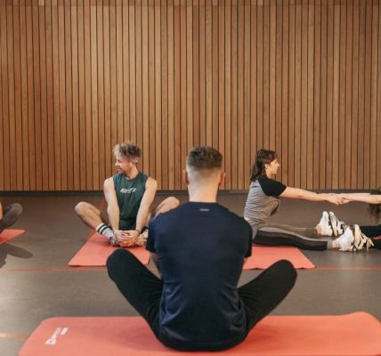 A group of adults practicing yoga and stretching on mats in a wooden panelled room.