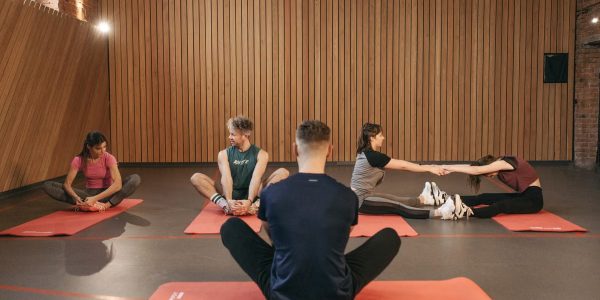 A group of adults practicing yoga and stretching on mats in a wooden panelled room.